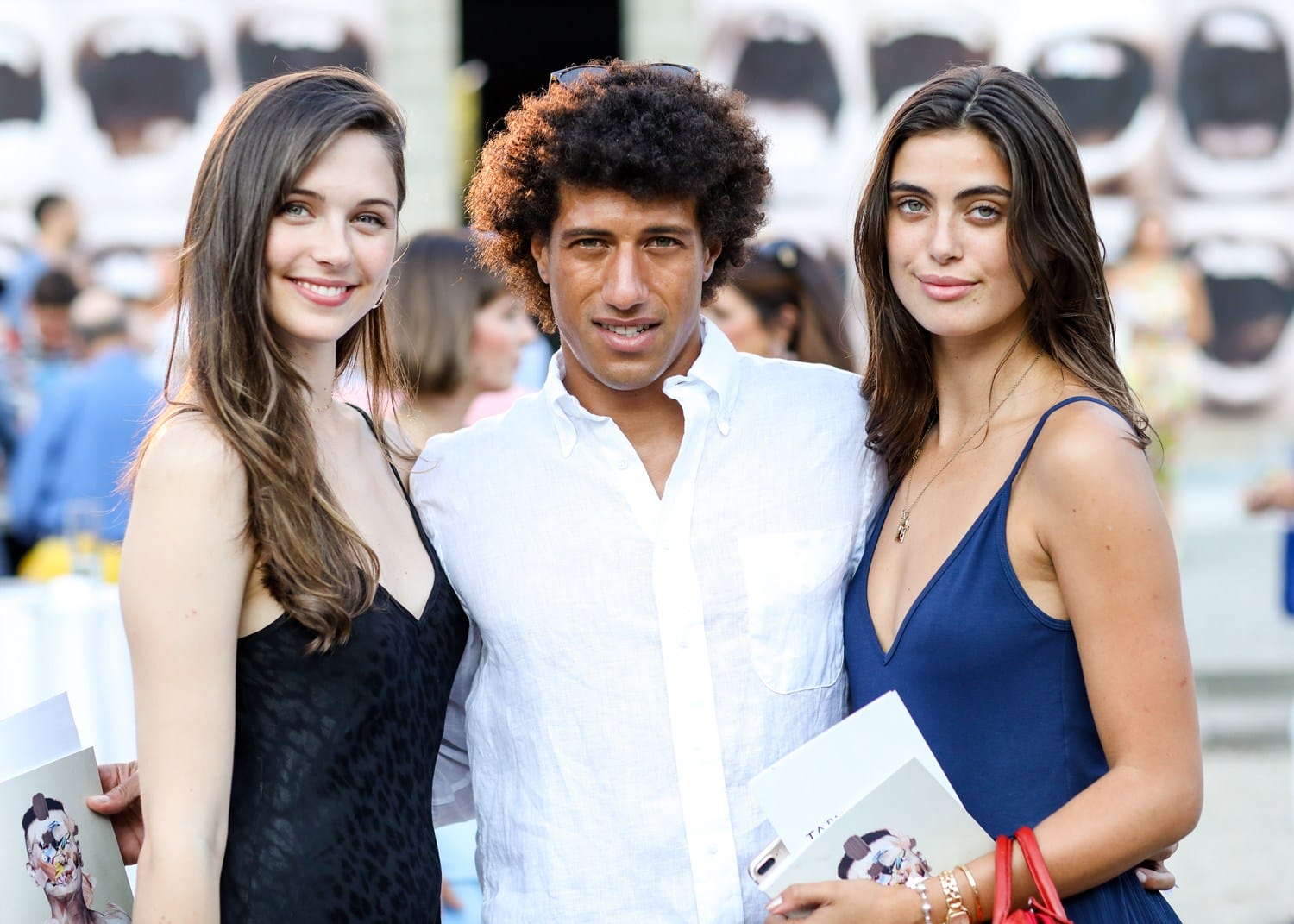 Three people posing together outdoors at an event, holding programs and smiling at the camera.