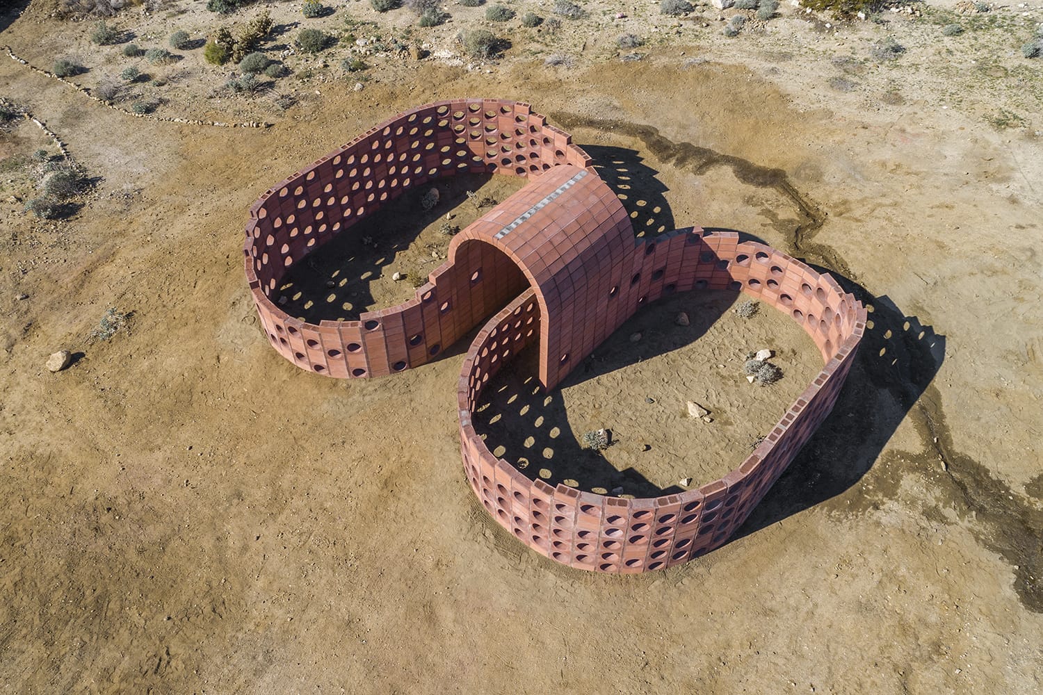 Aerial view of a brick building with an infinity-shaped design on a barren landscape.
