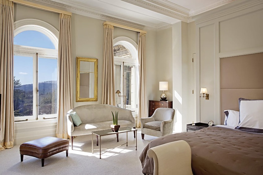 Spacious, elegantly decorated bedroom with large windows, a comfortable bed, and seating area with a sofa and chair.