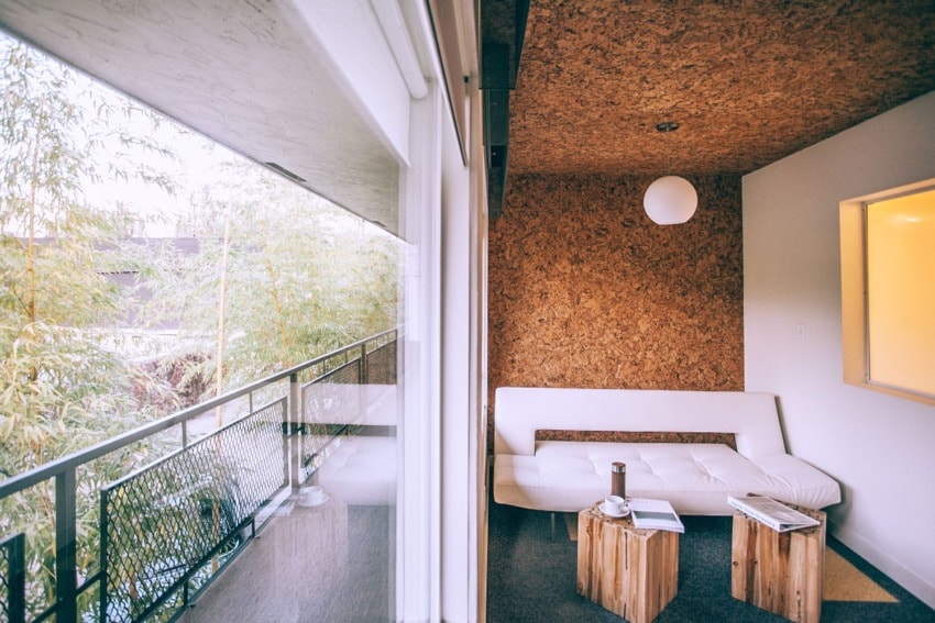 Modern living room with white sofa, wooden coffee tables, and large window overlooking a balcony with greenery.