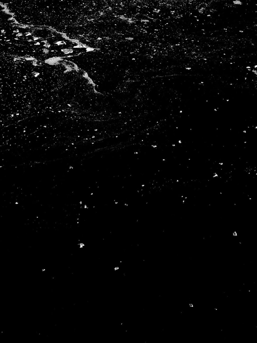 White specks scattered on a textured black surface, resembling a celestial pattern in a dark sky.