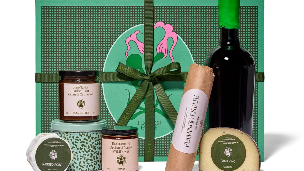 Gift box with wine, cheese, honey, pear butter, and luxury food items set against a green decorative backdrop.