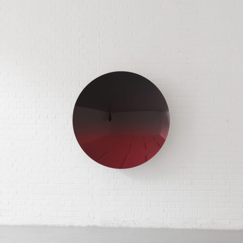 Circular black and red mirror art piece hanging on a white brick wall.