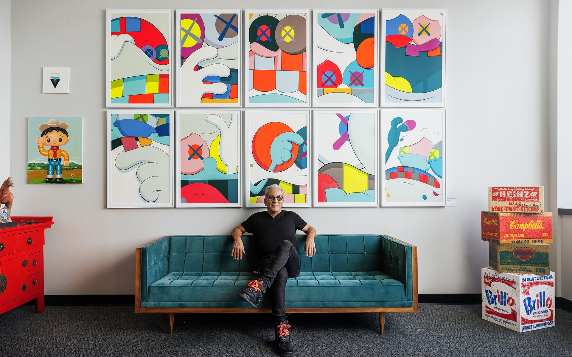 Person sitting on a teal sofa in front of colorful abstract artwork, surrounded by vintage pop art items.