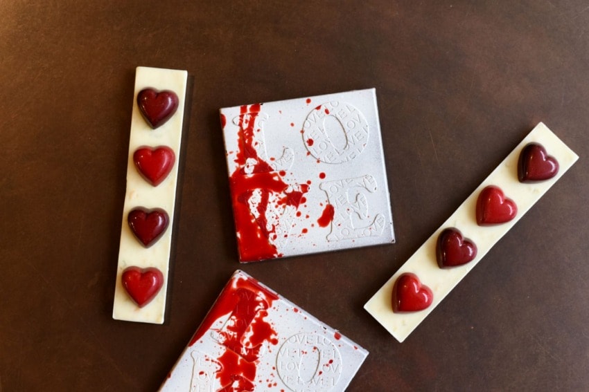 White chocolate bars with red heart decorations and artistic red splatters on a dark brown surface.