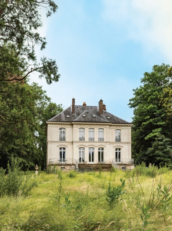 Elegant historic white mansion surrounded by lush greenery against a blue sky background