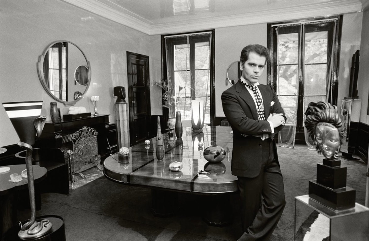 Person in a suit standing with arms crossed in an elegantly decorated room with art and modern furniture.