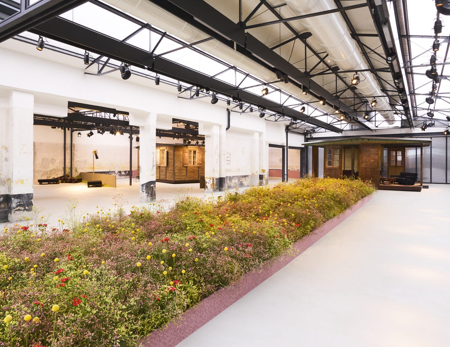 Spacious interior of a modern exhibition hall with floral installations and industrial architecture elements.