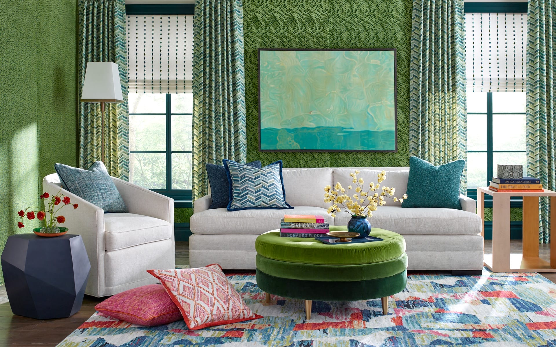 Colorful living room with a white sofa, green ottoman, patterned pillows, and artwork on a green accent wall.