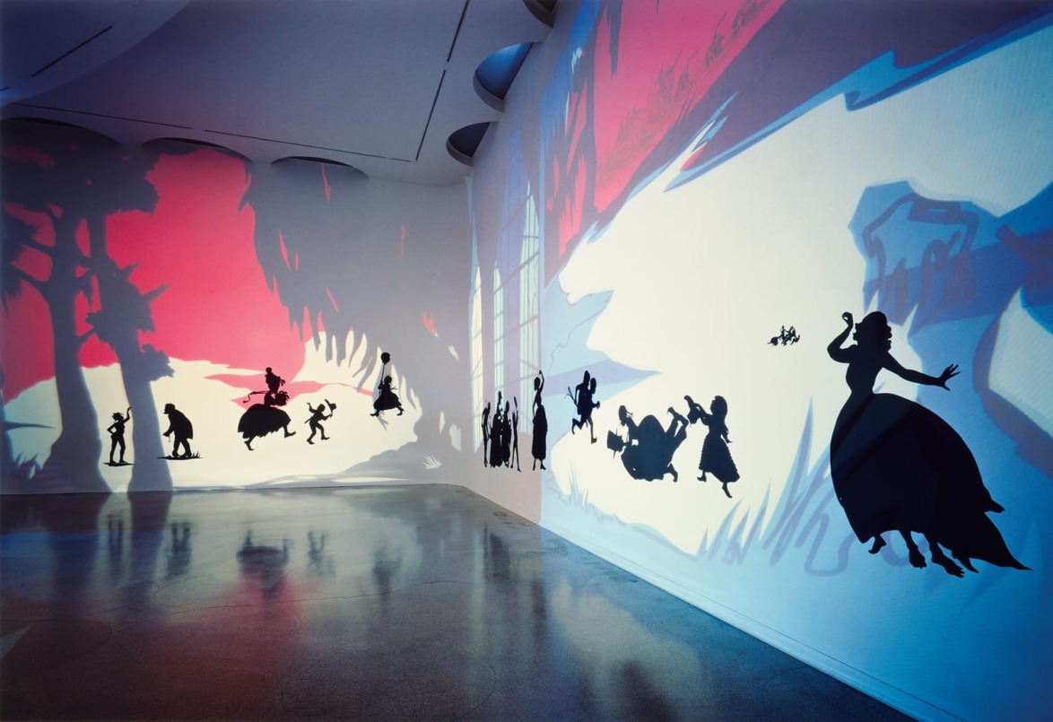 Art installation with colorful shadows on a white gallery wall, featuring silhouettes of people in various playful poses.