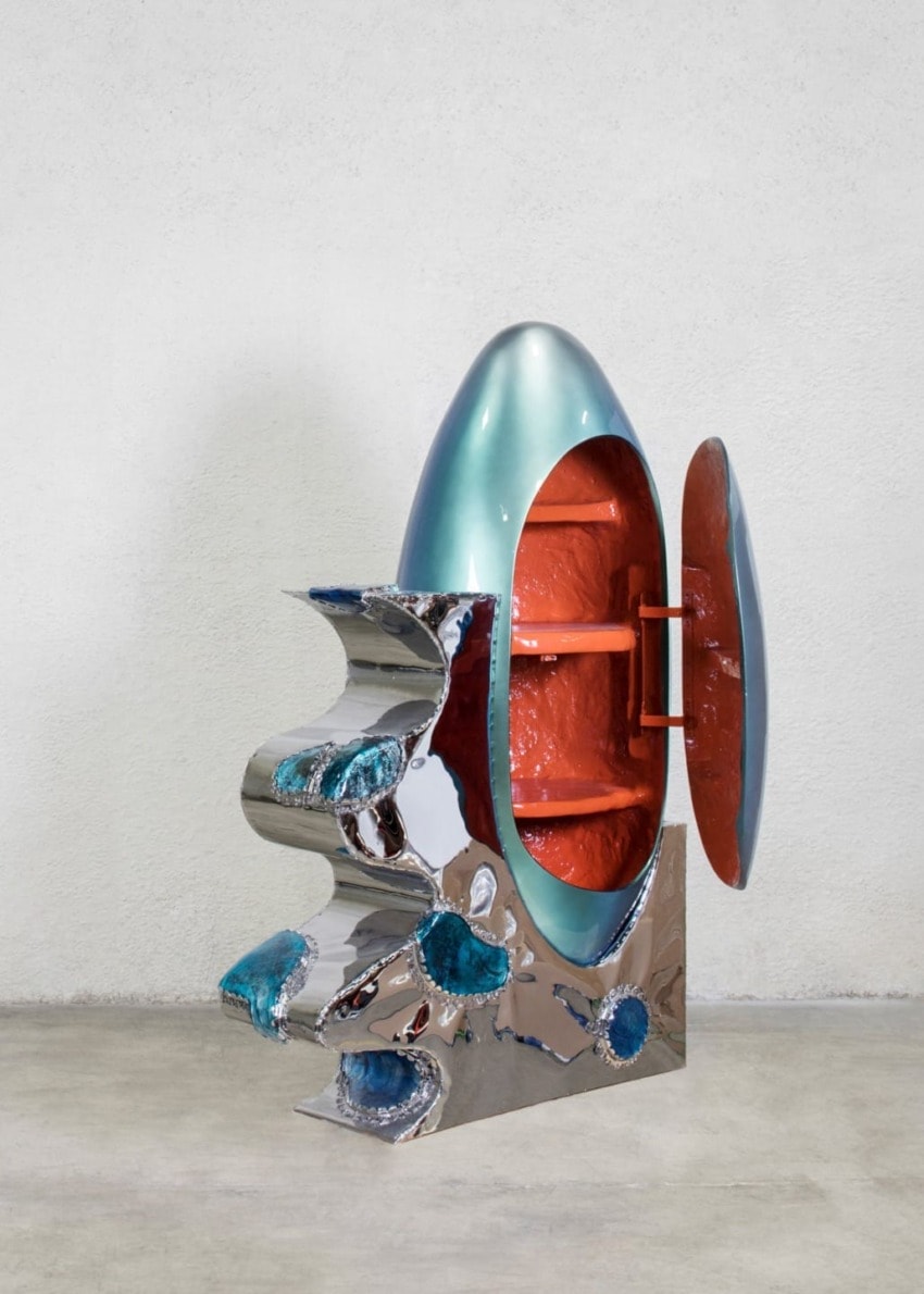 Futuristic, artistic cabinet with a metallic finish and an open door revealing orange interior shelves, set against a plain backdrop.