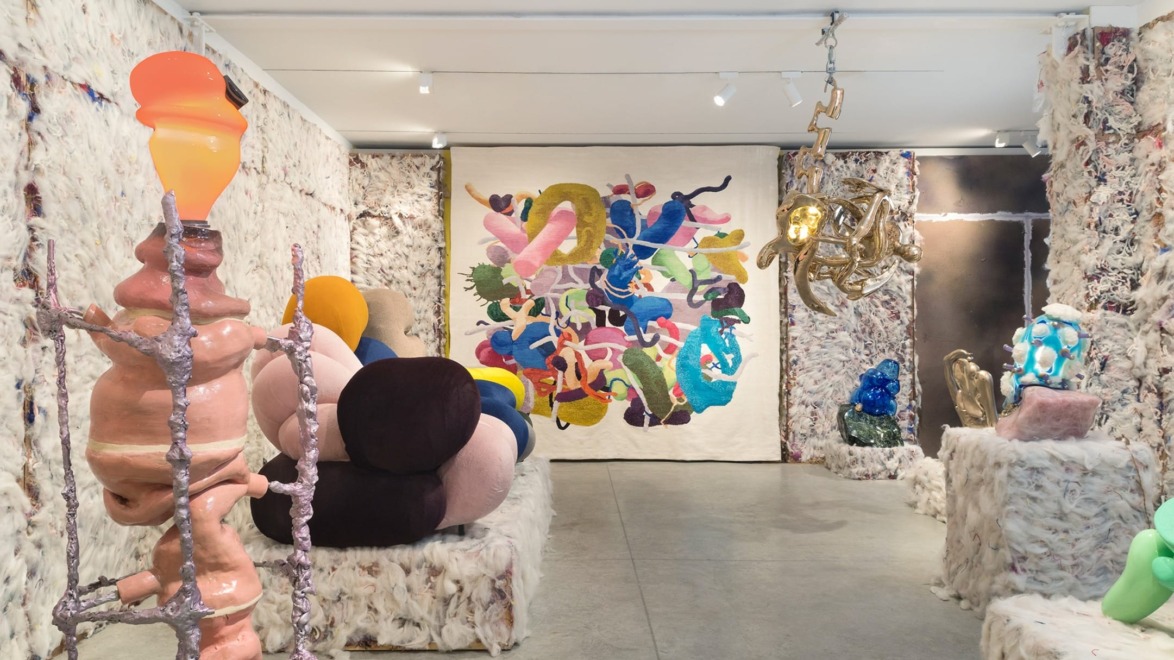 Contemporary art gallery exhibition with colorful abstract sculptures and a vibrant textile piece on the wall.