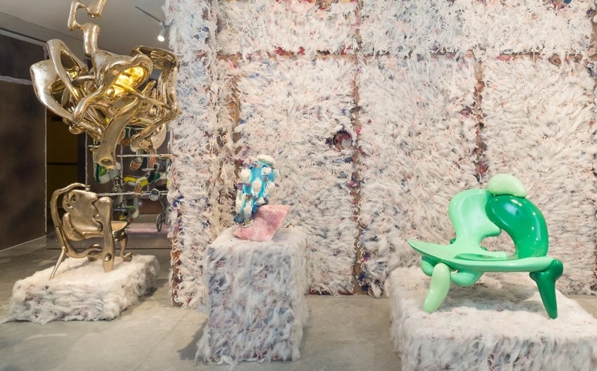 Colorful abstract sculptures displayed on pedestals with textured wall background in art exhibition setting.