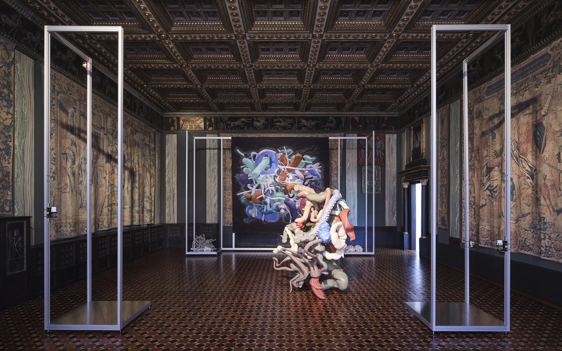 Contemporary abstract sculpture in a grand, ornately decorated room with detailed ceiling and intricate wall tapestries.