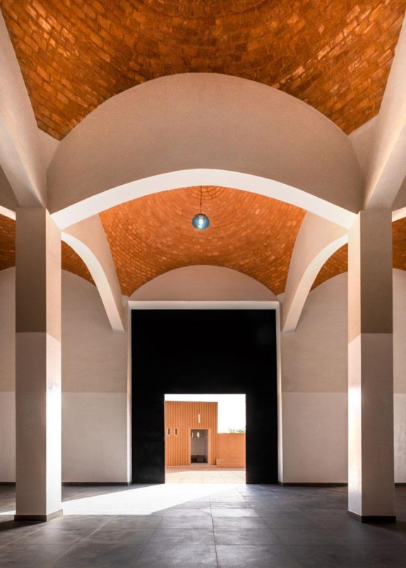 Interior of a modern building with arched brick ceiling, large doorway, and tiled floor lit by natural light.