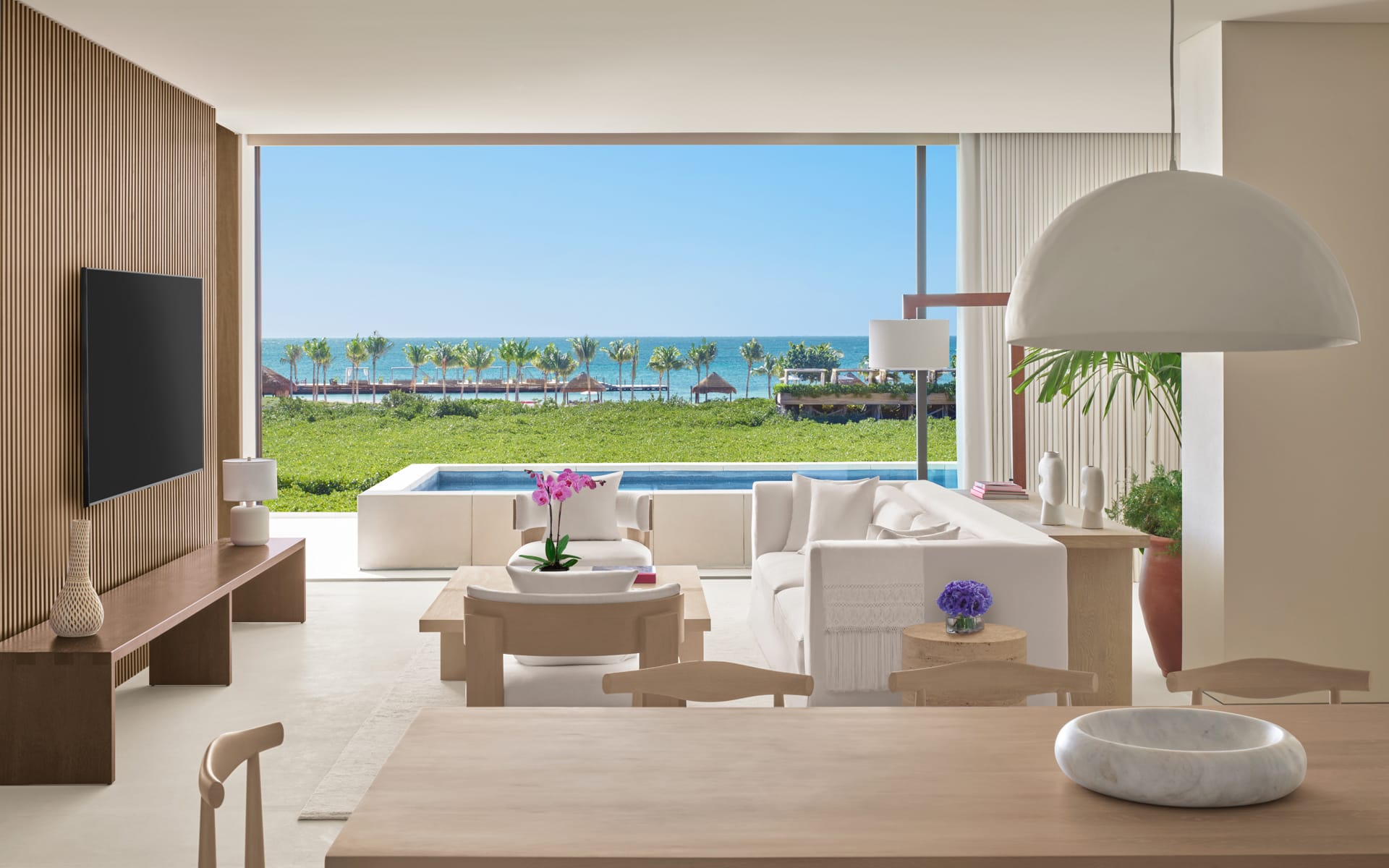Luxurious open-plan living room with modern furnishings, spacious terrace, and ocean view overlooking a pool.