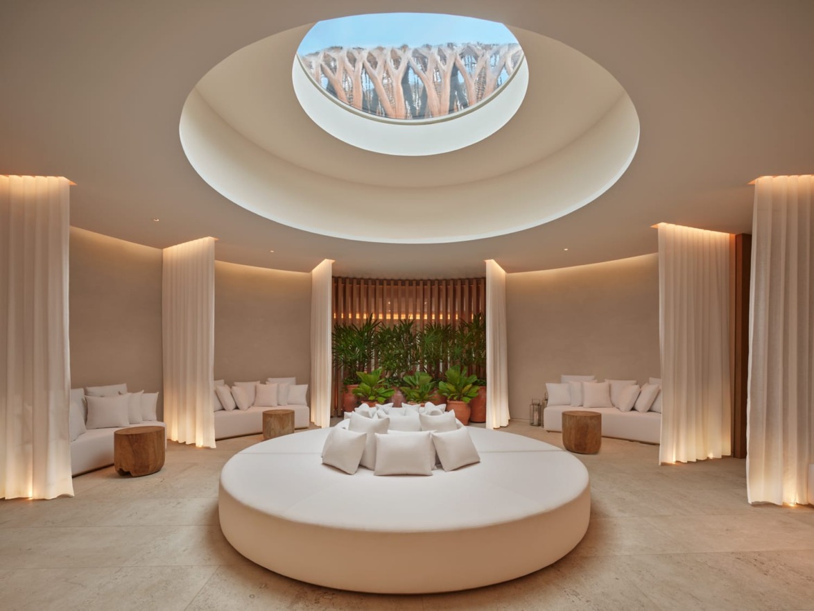 Modern circular lounge with skylight, white sofas, and wooden accents, creating a serene and inviting atmosphere.