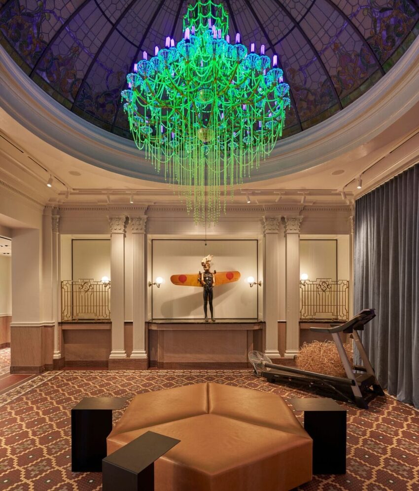 Luxurious room with a green chandelier, elegant decor, and a modern artwork display under a stained-glass dome ceiling.