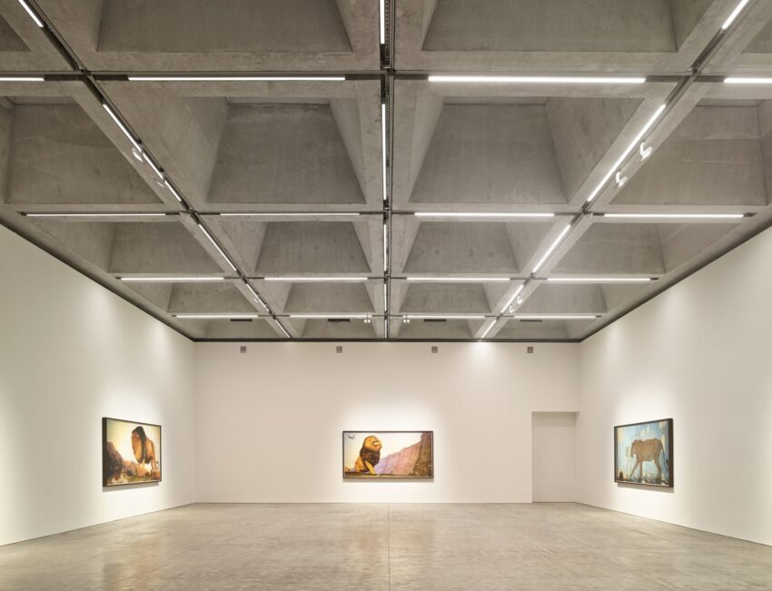 Modern art gallery with concrete ceiling, displaying three large framed paintings on white walls, minimalist design.