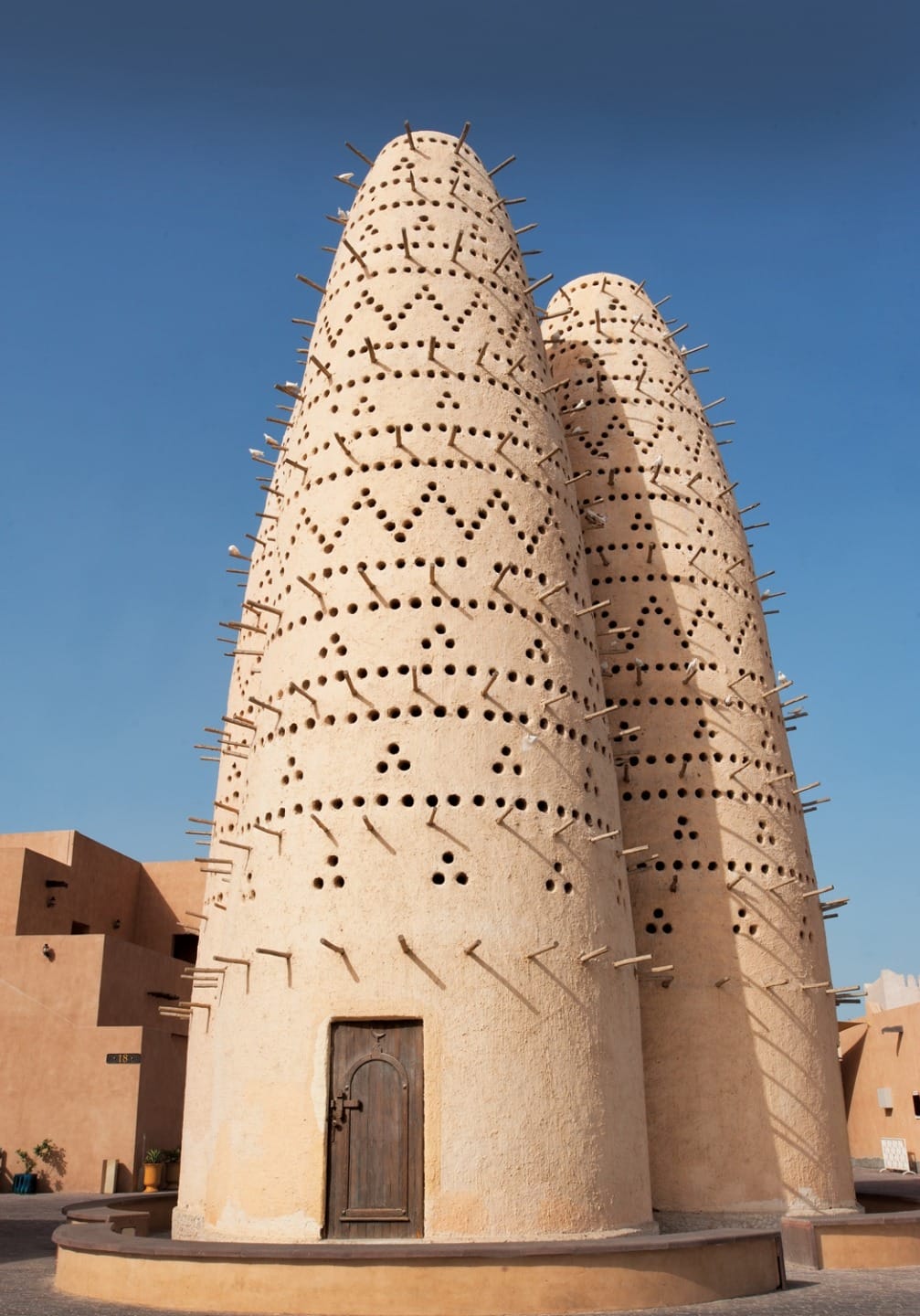 Two traditional Middle Eastern pigeon towers with intricate patterns, set against a clear blue sky.