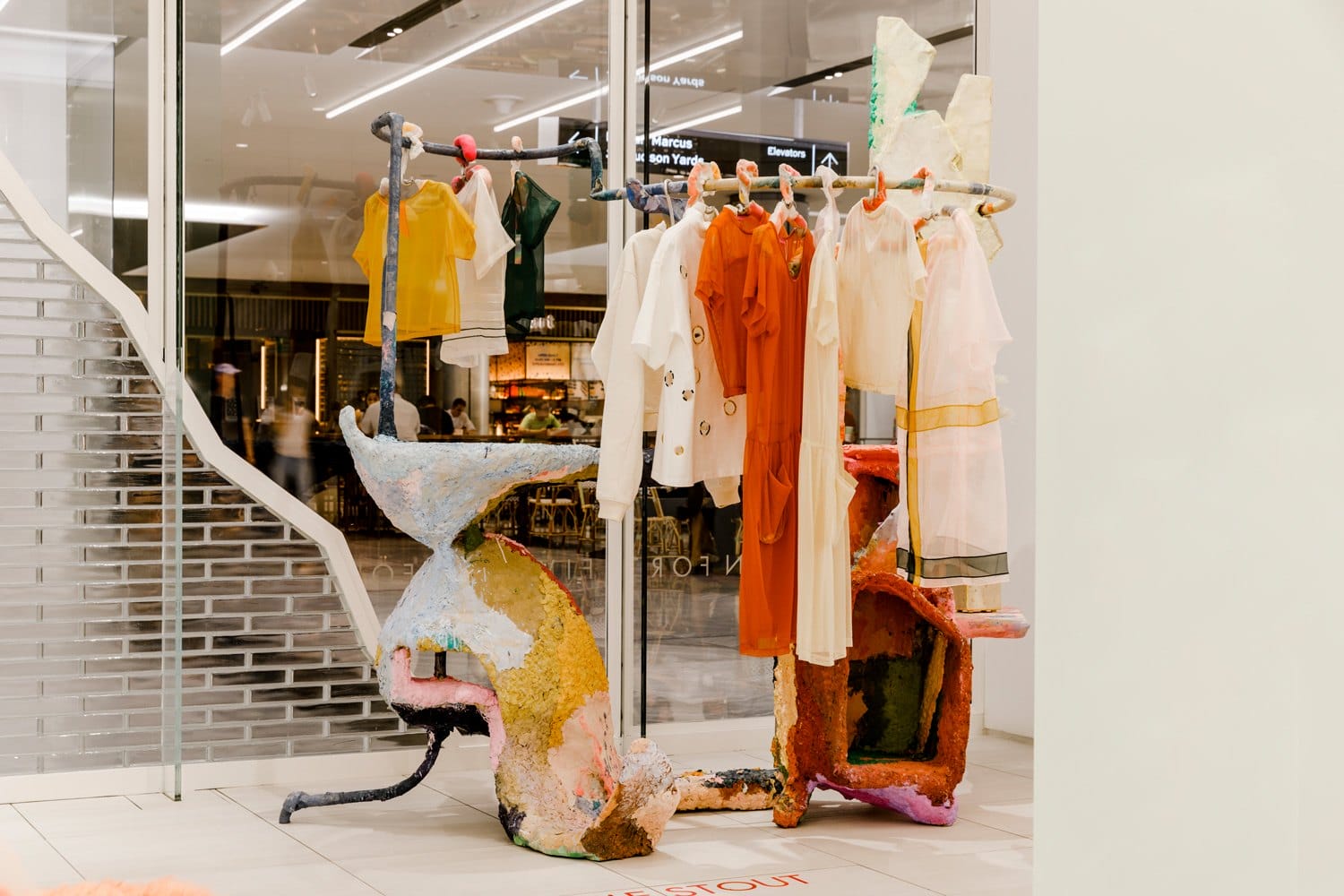 Colorful fashion display with unique sculpture-like hangers showcasing various stylish clothes in a modern retail setting.