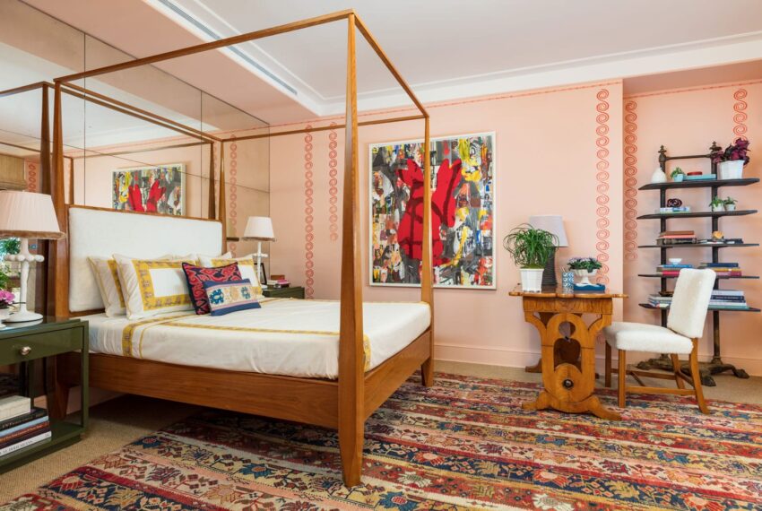 Brightly decorated bedroom with a wooden canopy bed, colorful rug, vibrant artwork, and a small desk with a chair.