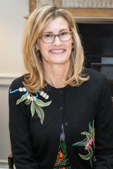 Person wearing glasses and a floral embroidered sweater, smiling in an indoor setting.