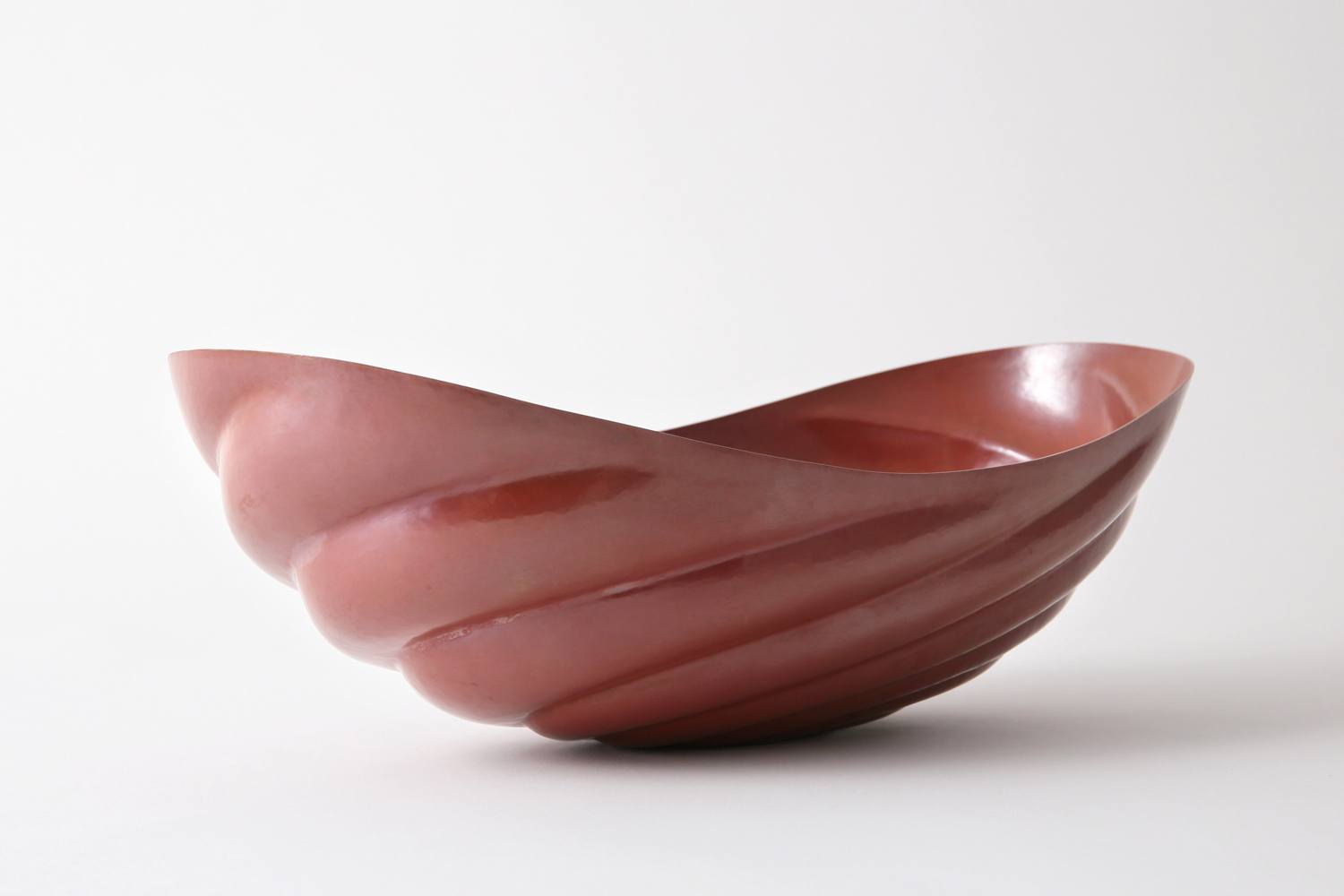 Sculptural maroon ceramic bowl with smooth, wave-like contours against a plain white background.