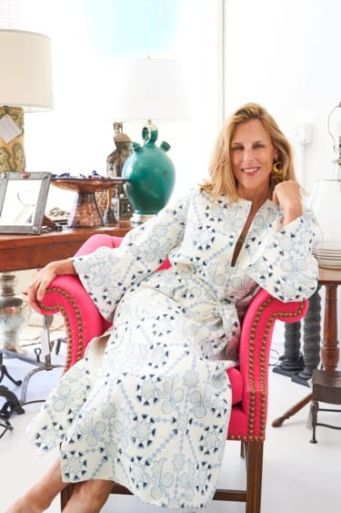 Person in a patterned robe sits on a pink chair in a room with eclectic decor.