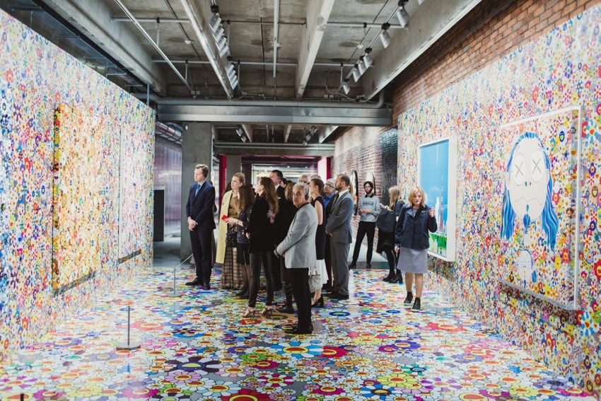 Group of people observing colorful floral art exhibits inside a modern gallery with vibrant patterned walls and floors.