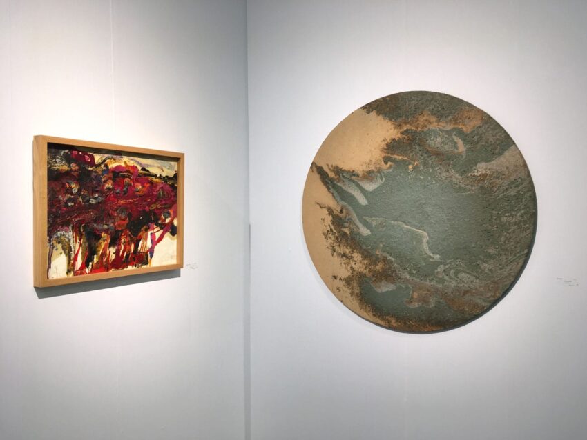 Abstract art pieces displayed on a gallery wall, one rectangular with red hues, the other circular with earthy tones.