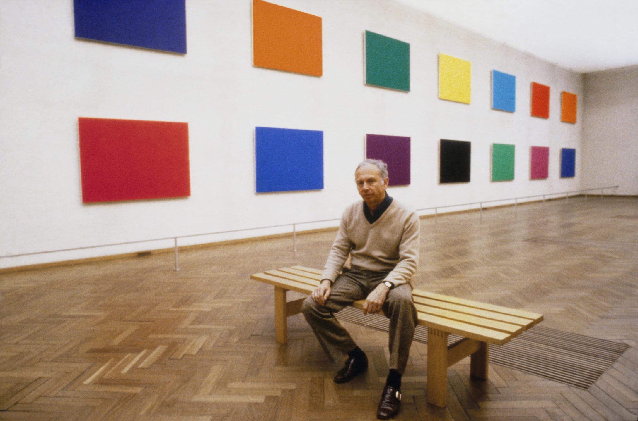 A person sitting on a bench in an art gallery with colorful abstract paintings on the walls.