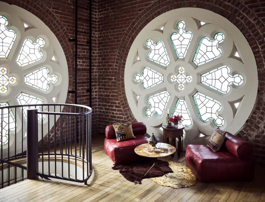 Loft interior with large circular stained glass windows, red leather chairs, a round coffee table, and wooden floors.