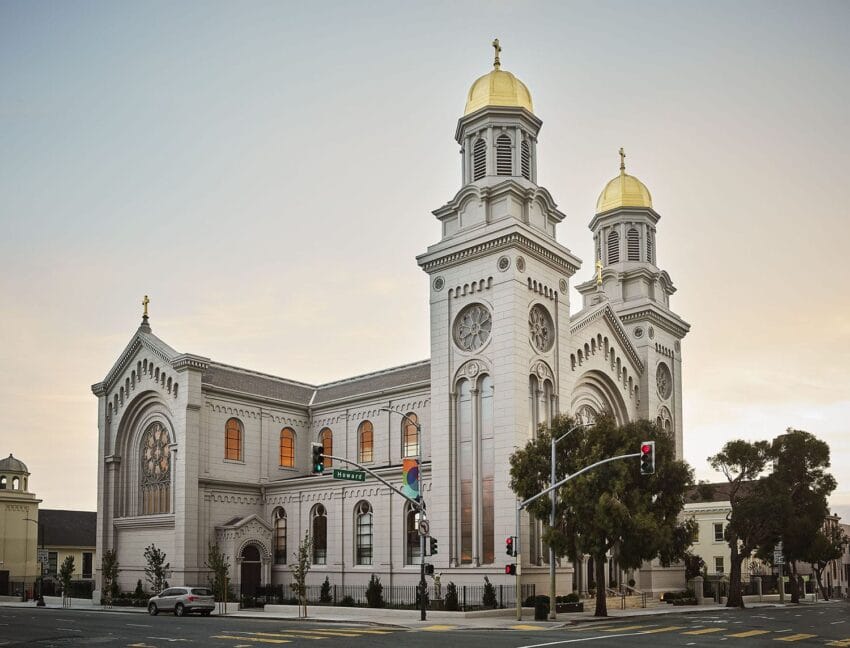 Exterior view of a large, historic church with two towers and golden domes at sunset.