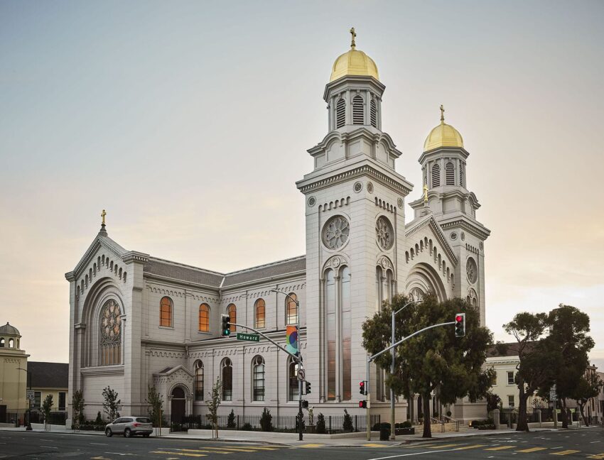 Exterior view of a large, historic church with two towers and golden domes at sunset.