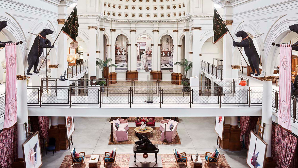 Grand hall interior with high ceiling, decorative banners, and seating area surrounded by paintings and sculptures.