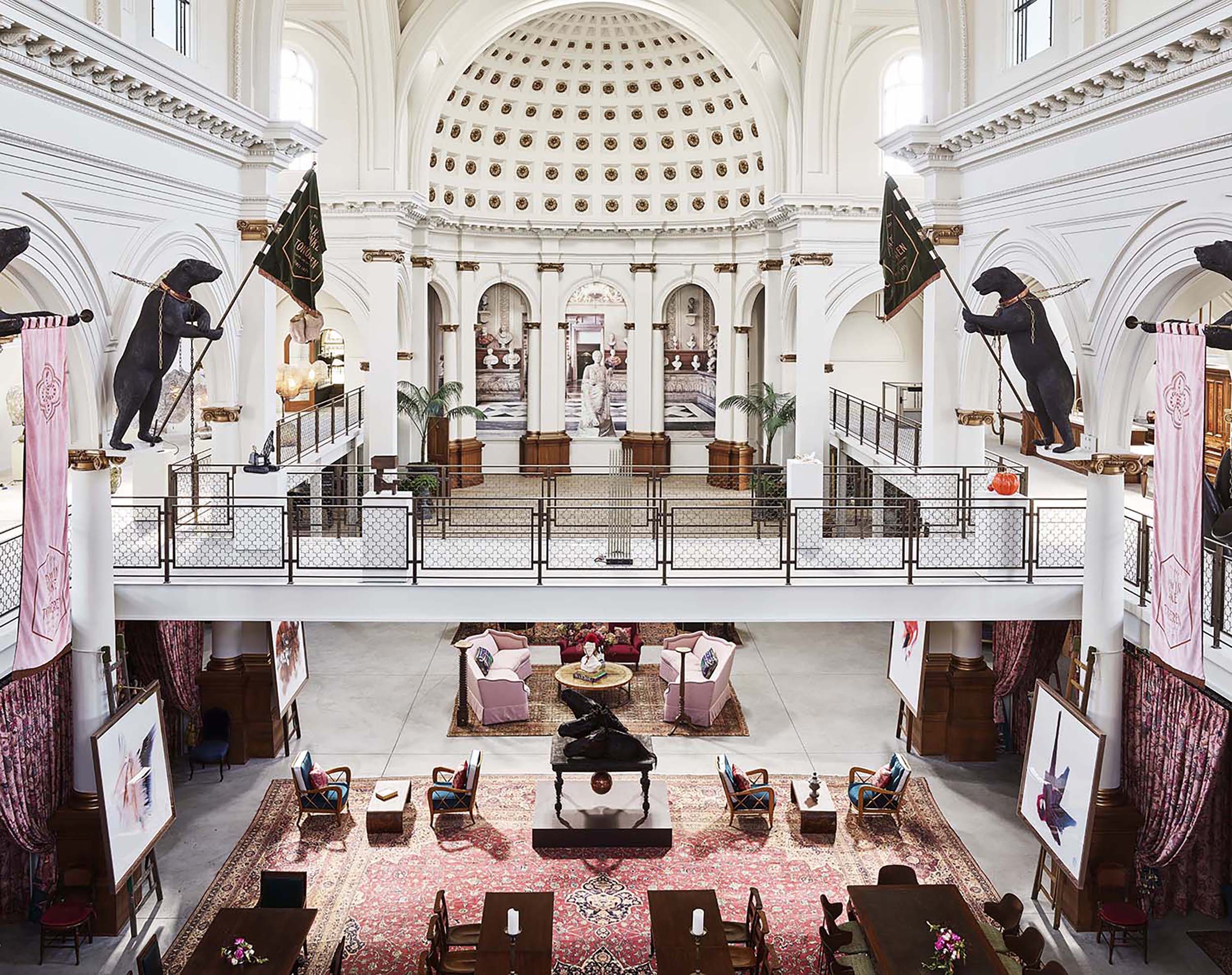 Grand hall interior with high ceiling, decorative banners, and seating area surrounded by paintings and sculptures.