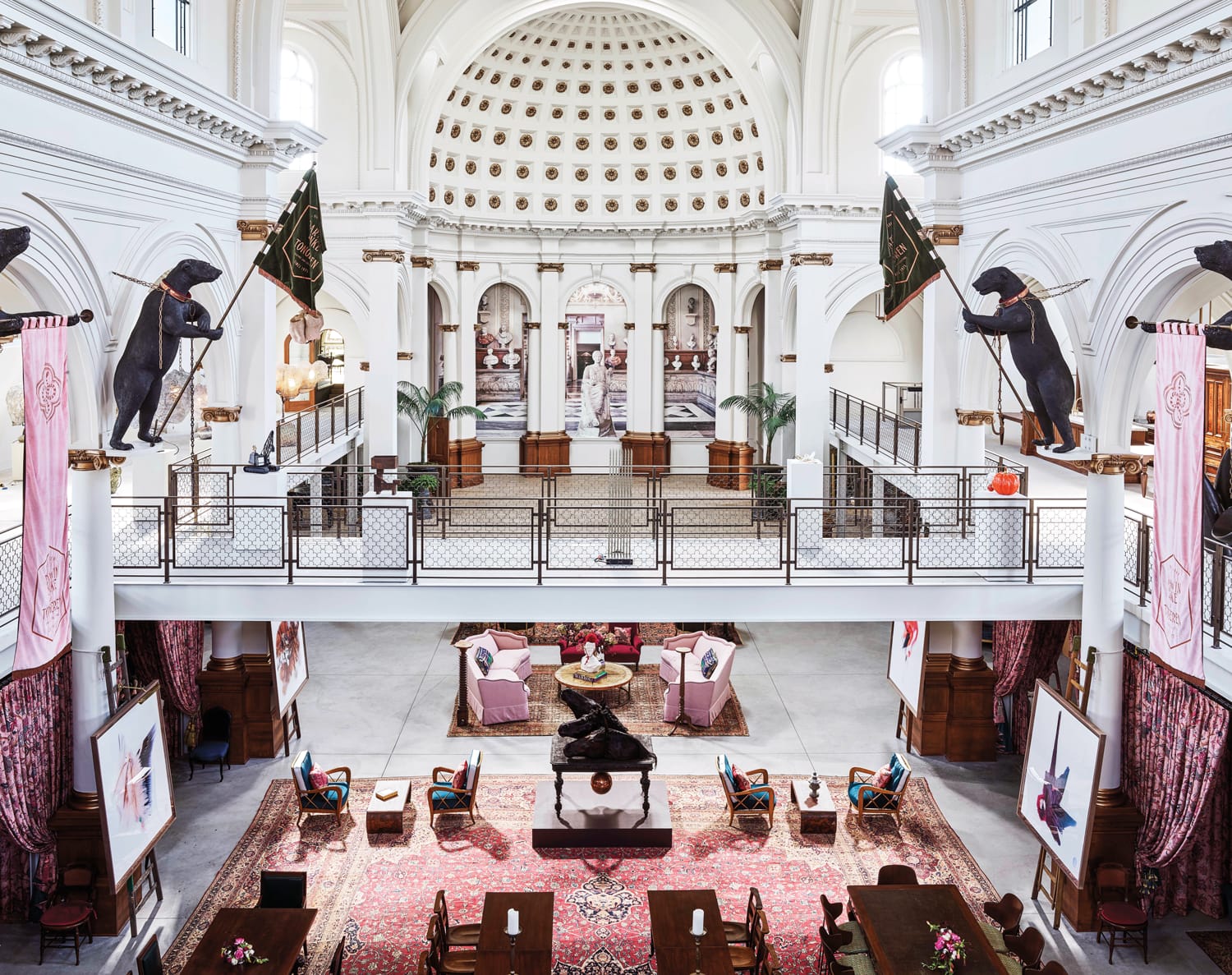 Grand library interior with high vaulted ceiling, statues, large rugs, seating areas, and ornate architectural details.
