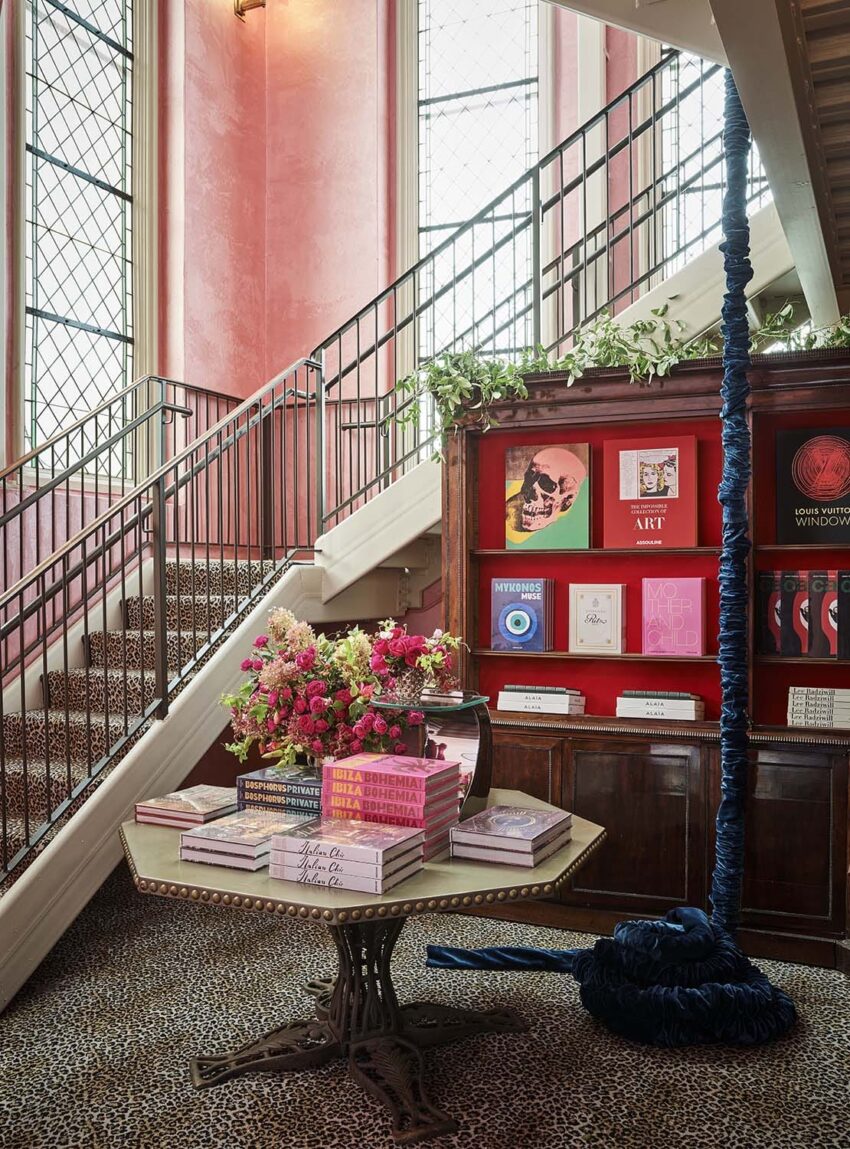 Elegant interior with a winding staircase, colorful books on a table, and a striking blue rope hanging from the ceiling.