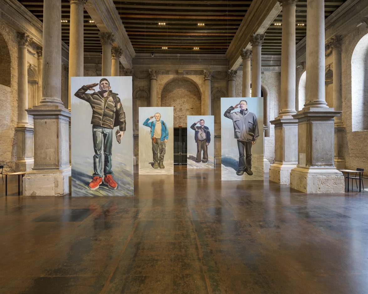 Art installation in a grand hall with pillar structures, featuring four large portraits of people saluting.