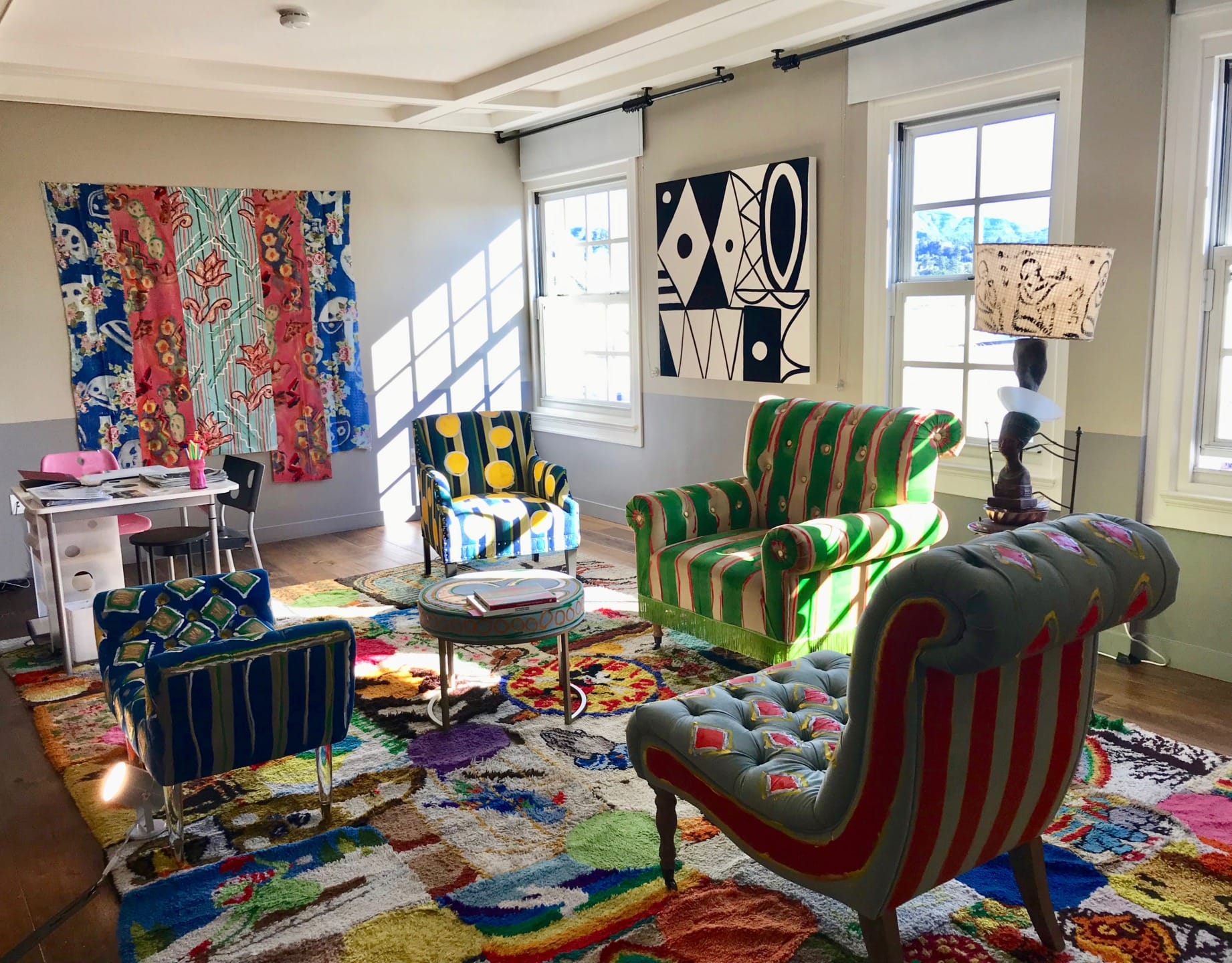 Colorful living room with patterned chairs, vibrant rug, and abstract wall art in a bright, sunlit space.