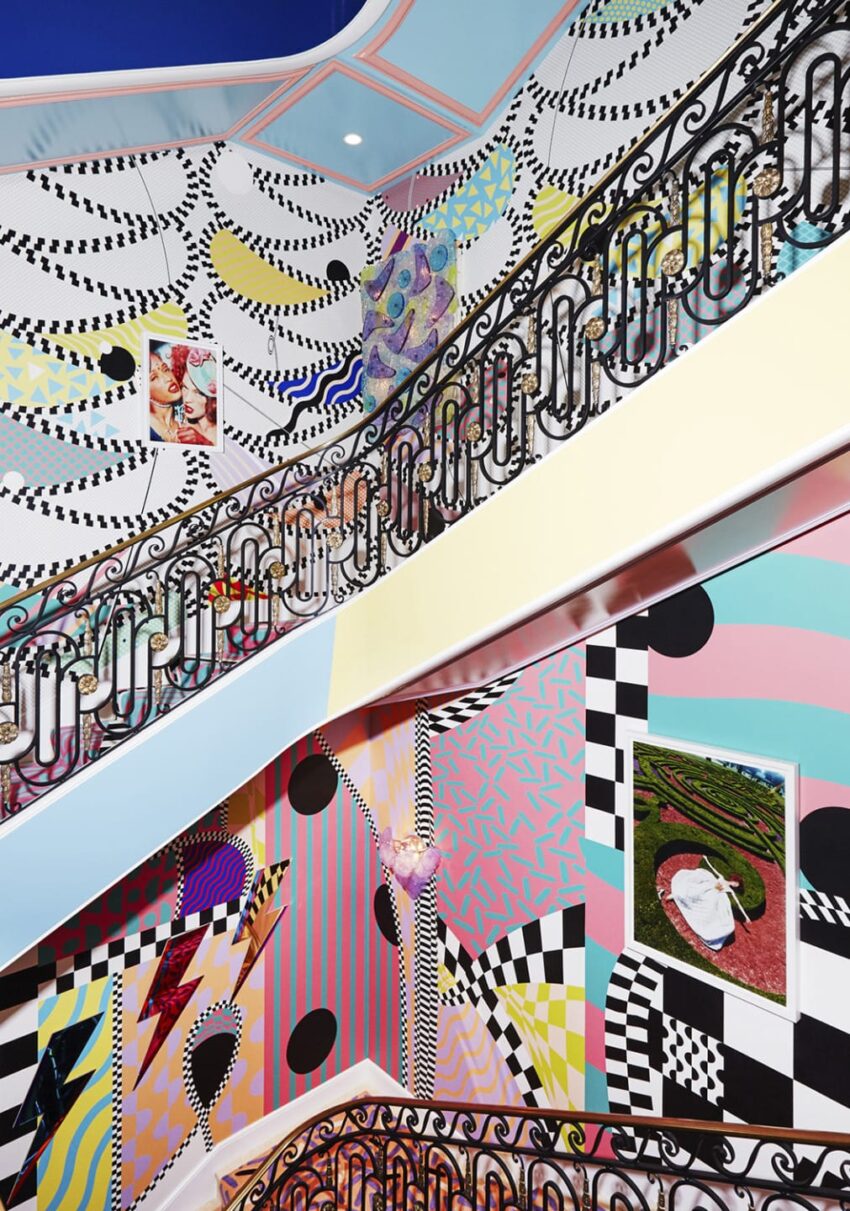 Colorful abstract art covers stairwell walls with geometric patterns and framed artwork on display.