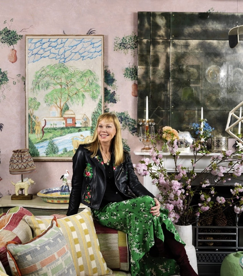 Woman in floral dress and leather jacket sitting on a couch in a stylish living room with art and decorative elements.