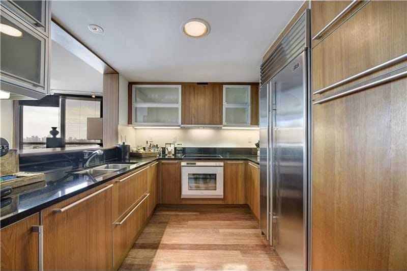 Modern kitchen with wooden cabinets, stainless steel appliances, black countertops, and large window for natural light.