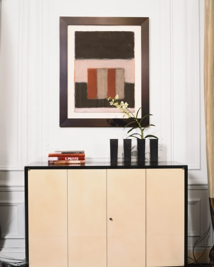Modern art piece above a light-colored cabinet with a black vase and a single stemmed flower, set in an elegant room.