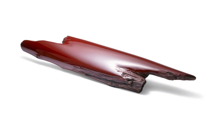 Glossy, smooth red surfboard with natural wood texture on one end, creating a blend of modern design and organic elements.