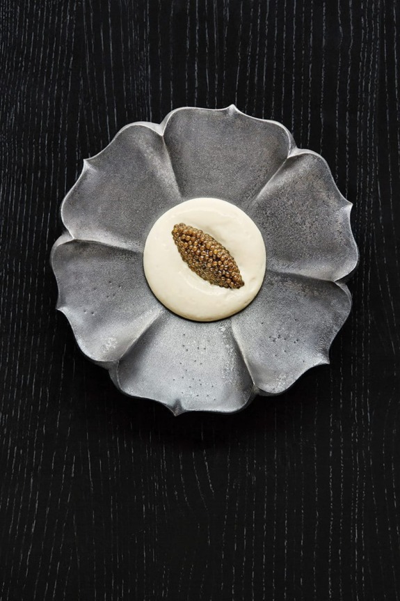 Silver plate with creamy dish topped with a spoonful of caviar, placed on a dark wood textured surface.
