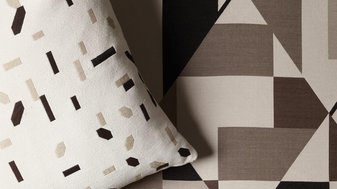 Geometric patterned fabric with abstract brown, black, and white shapes, including a pillow featuring similar designs.