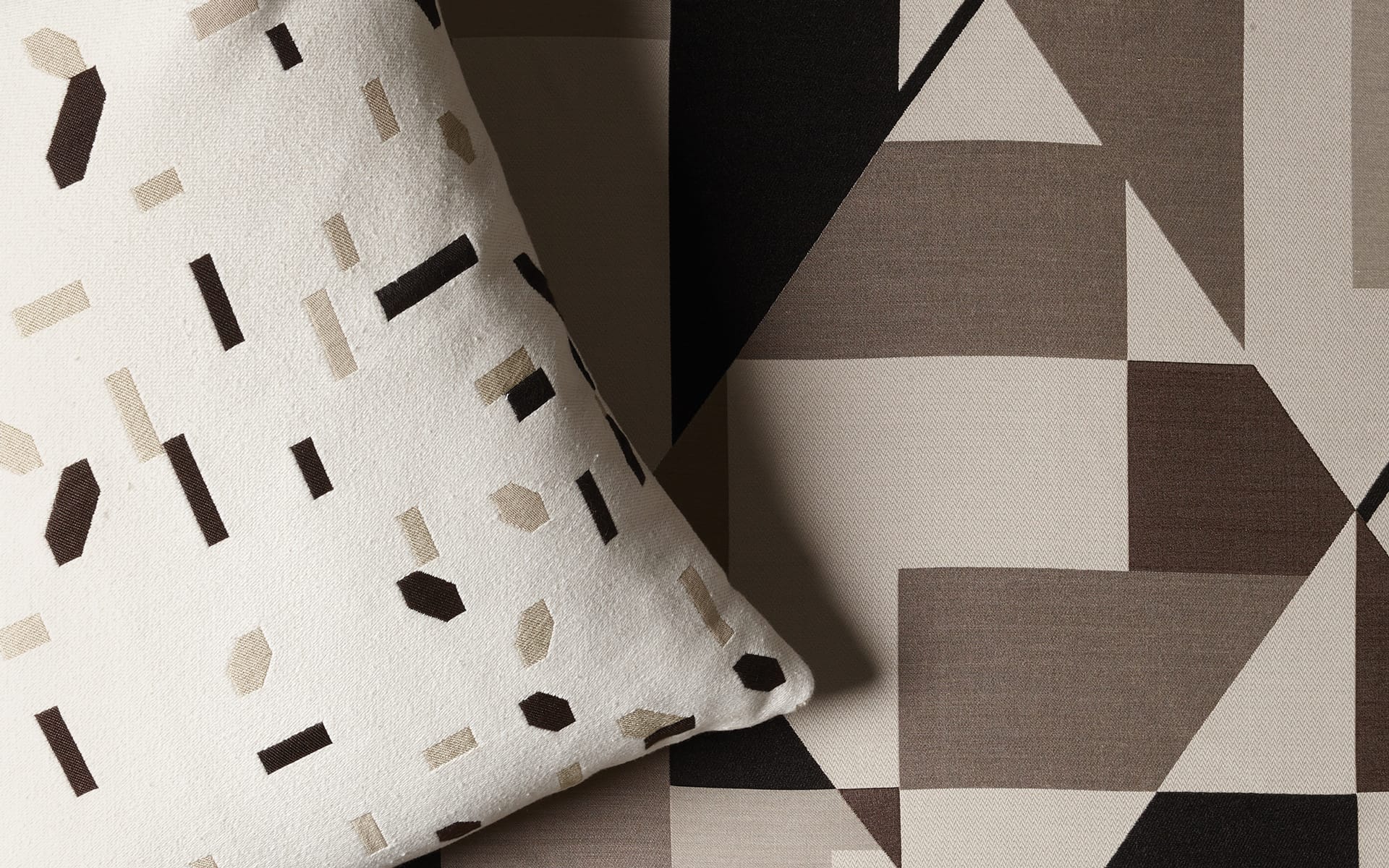 Geometric patterned fabric with abstract brown, black, and white shapes, including a pillow featuring similar designs.
