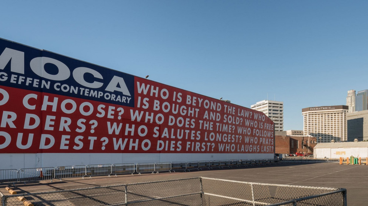 MOCA mural in Los Angeles with red and white text posing questions about law, choice, and authority, against blue sky.